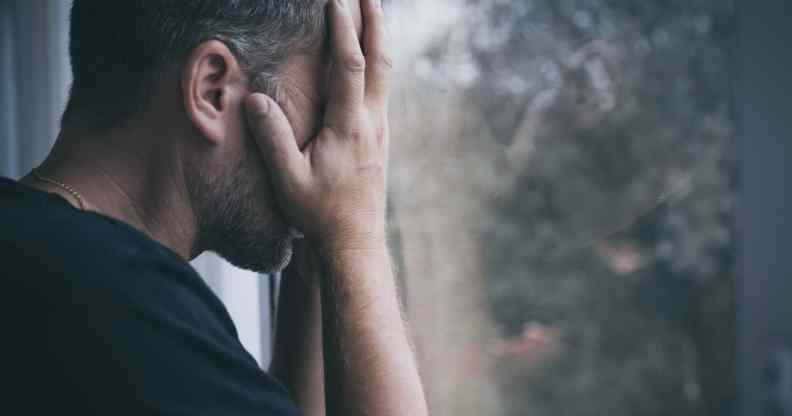 Man standing near a window and covers his face