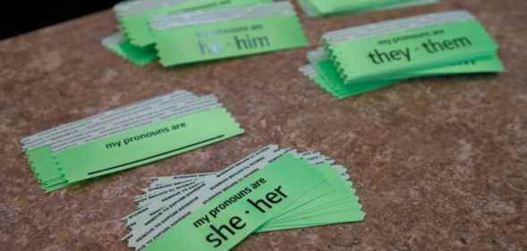 Pronoun stickers on a table, reading 'she/her', 'he/him', and 'they/them' along with blank ones