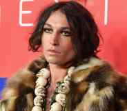 Actor Ezra Miller wears a fluffy brown fur-like jacket with a skull necklace and shiny makeup