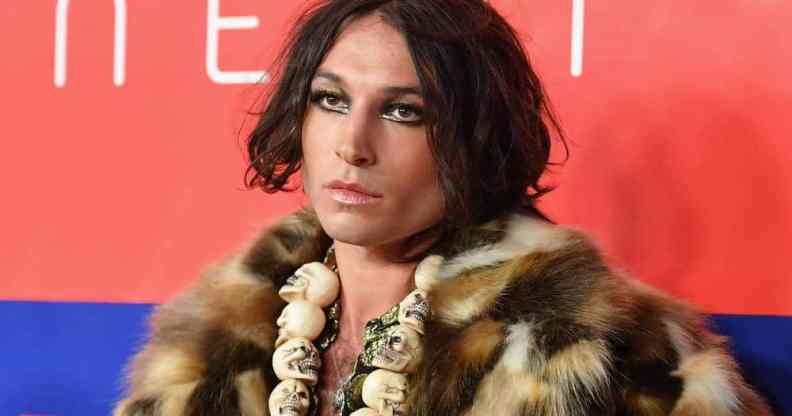 Actor Ezra Miller wears a fluffy brown fur-like jacket with a skull necklace and shiny makeup