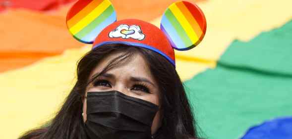 A woman wears Mickey Mouse ears with the Pride colours