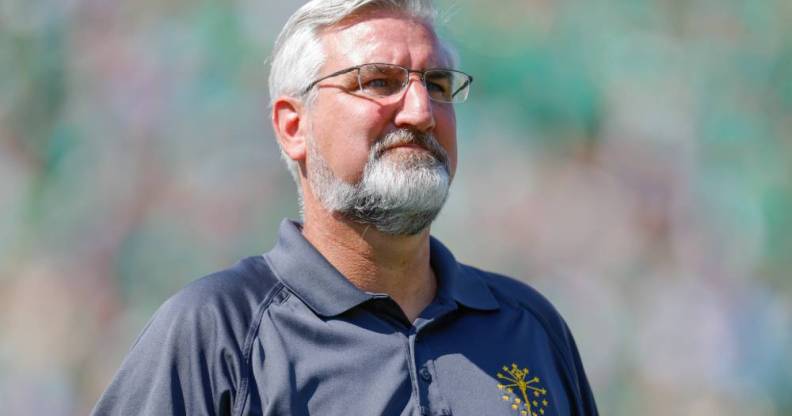 Eric Holcomb, the governor of Indiana, wears a blue polo shirt with a gold logo over his left chest