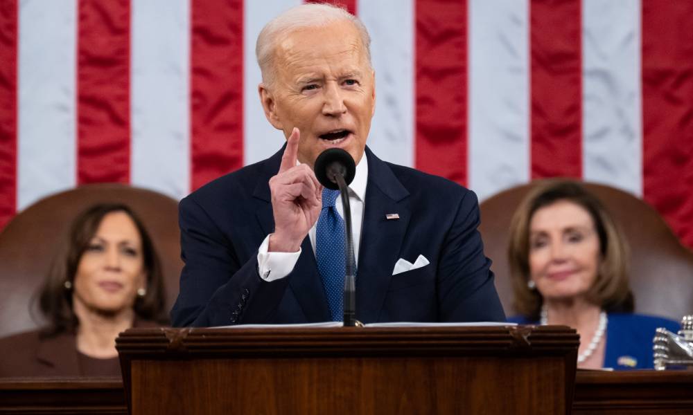 President Joe Biden stands at a podium to deliver his State of the Union address with an American flag in the background