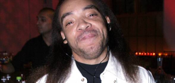 Kidd Creole, a rapper, smiles at the camera while wearing a black top and white jacket