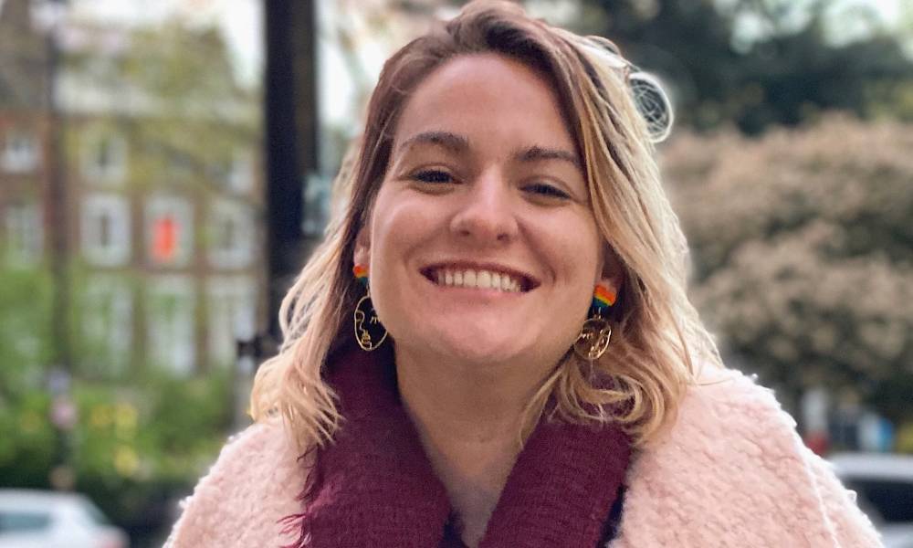 Tea Kane wears a pink fuzzy coat with a red coloured scarf as they smile at the camera