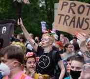 Person stands up during a protest with a sign reading "protect trans youth" in the background