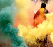 A person stands among multicoloured smoke