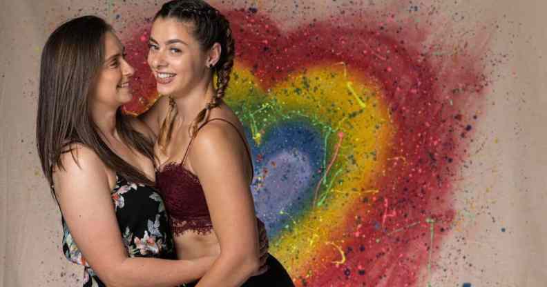 Jetta and Charlie Morgan, a British LGBT+ couple and wrestlers, hold each other close with a rainbow heart in the background