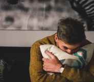 A man hugs a pillow in a bedroom