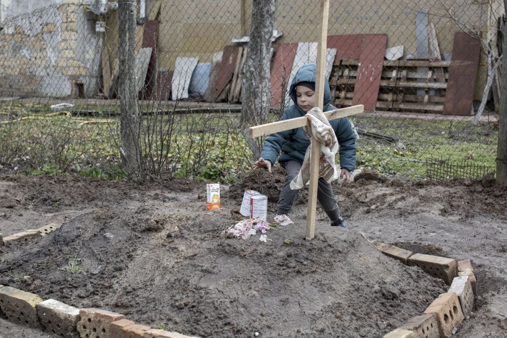 A child gives an offering of food to the grave of a woman in the town of Bucha, on the outskirts of Kyiv. 