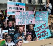 Crowd of people gather in protest of the UK government's U-turn on conversion therapy ban and hold up signs in support of protections for the trans community