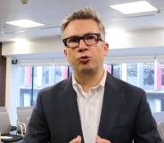 Iain Anderson wears a white shirt and black suit jacket as he looks at the camera