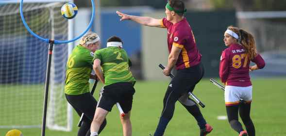 A real game of quidditch - here are four players with sticks between their legs (like broomsticks), one is jumping while throwing a ball into a hoop