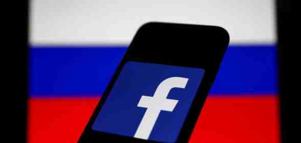 Facebook logo displayed on a phone screen and Russian flag displayed on a screen in the background