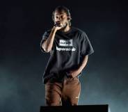 Kendrick Lamar raps on stage while wearing a black shirt and a brown pants