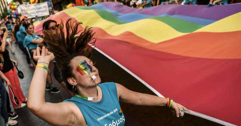 A participant dances while holding a large rainbow flag during the Athens Gay Pride