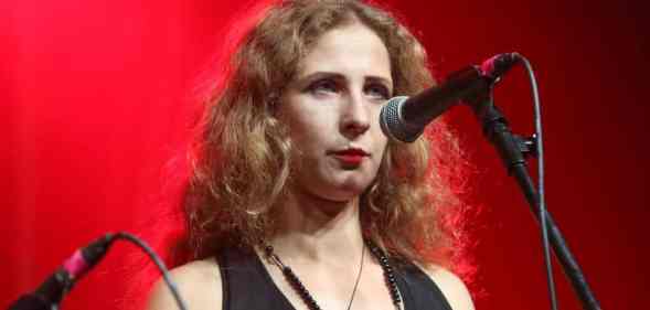 Pussy Riot leader Maria Alyokhina stands in front of a microphone with a red light and background