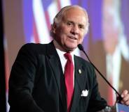 South Carolina governor Henry McMaster wears a white shirt, red tie and dark suit jacket as he speaks into a microphone on stage