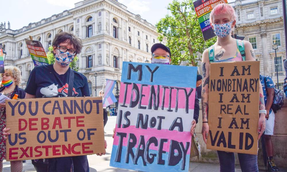 several people hold up signs during a trans rights protest one reads "you cannot debate us out of existence", "my identity is not a tragedy" and "I am non-binary, I am real, I am valid"