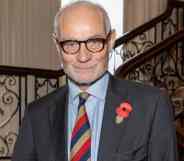 Conservative MP Crispin Blunt stands on a stair case wearing a dark suit jacket, light blue shift and a red, yellow and dark blue striped tie