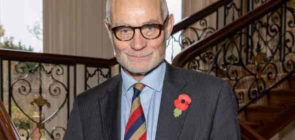 Conservative MP Crispin Blunt stands on a stair case wearing a dark suit jacket, light blue shift and a red, yellow and dark blue striped tie