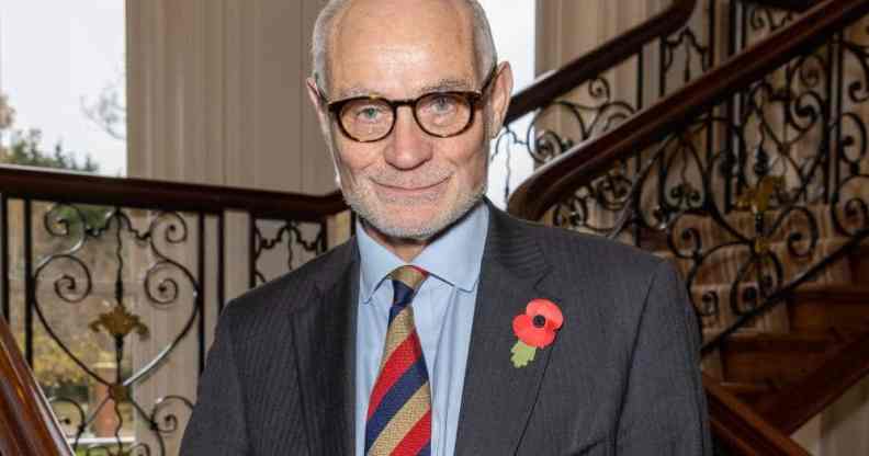 Conservative MP Crispin Blunt stands on a stair case wearing a dark suit jacket, light blue shift and a red, yellow and dark blue striped tie