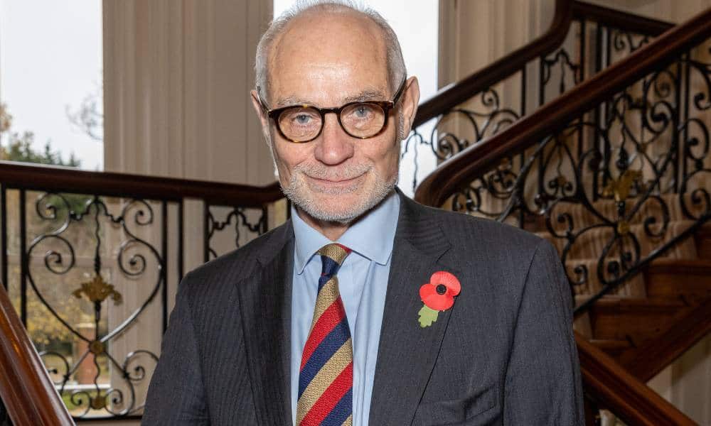 Conservative MP Crispin Blunt stands on a stair case wearing a dark suit jacket, light blue shift and a red, yellow and dark blue striped tie