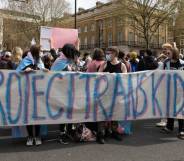 A group of people hold up a sign that reads 'protect trans kids' in blue and pink