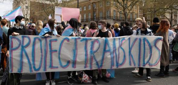 A group of people hold up a sign that reads 'protect trans kids' in blue and pink