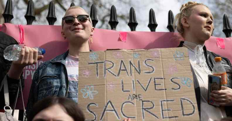 two people hold up a sign that reads 'trans lives are sacred'