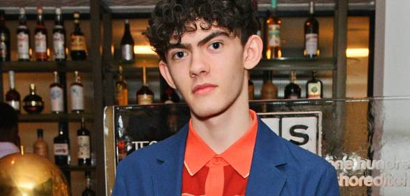 Heartstopper star Joe Locke stares at the camera while wearing an orange patterned shirt and blue jacket