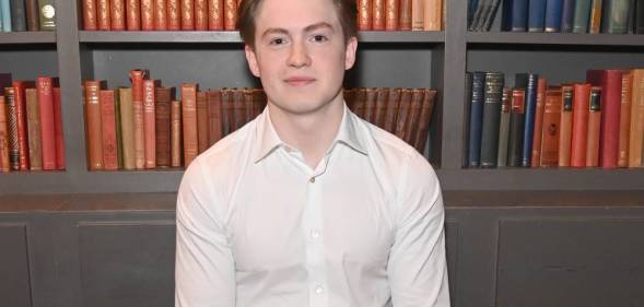 Kit Connor poses in the green room that appears to have books in it