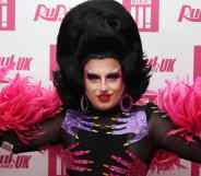 Drag Race UK star Choriza May stares at the camera while wearing a black wig, black outfit with pink and purple hands on it