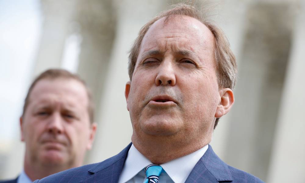 Republican Texas attorney general Ken Paxton wears a white shirt, blue suit jacket and tie as he speaks to someone off camera