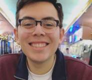 Julio Ramirez is seen smiling at the camera while wearing a black and red jacket with a white shirt and wearing black rimmed glasses