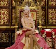 Drag Race UK queen River Medway appears wearing a peach and red coloured gown with a crown on her head while sitting on a gold throne