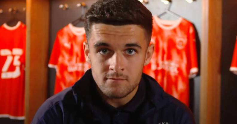 Blackpool football star Jake Daniels stares at the camera with football uniforms in the background