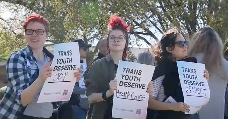 three people hold up signs that read "trans youth deserve joy", "trans youth deserve healthcare" and "trans youth deserve respect"