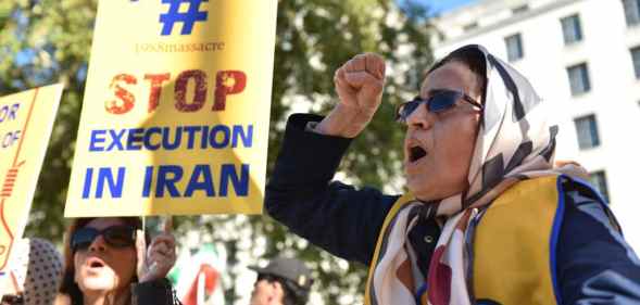 A woman shouting with her first in the air, a person next to her holds a placard that reads 'stop execution in Iran'