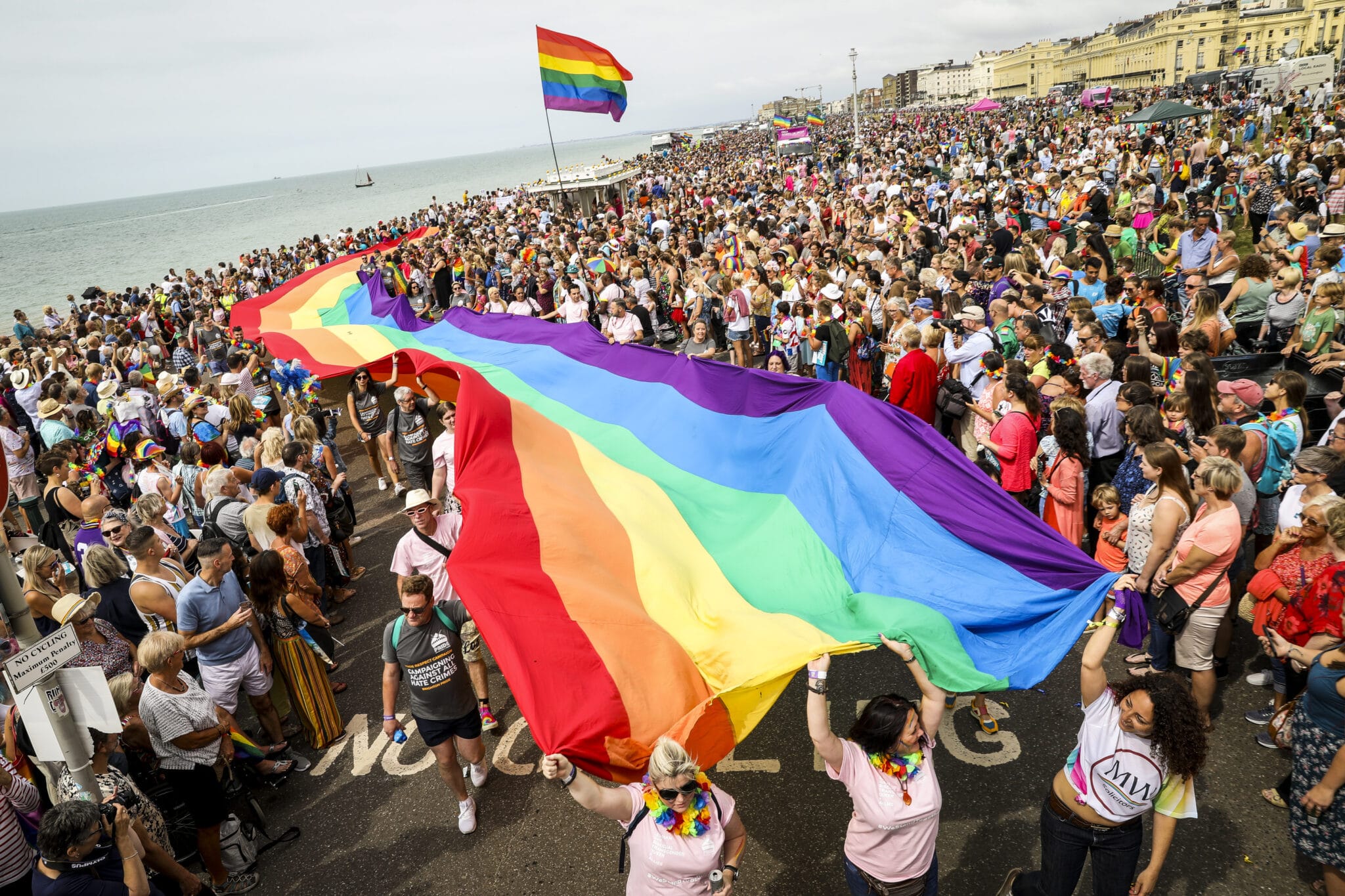 Pride revellers holding a giant flag with the rainbow colours. 