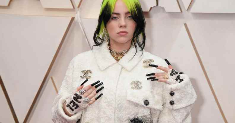 Singer Billie Eilish at Oscars 2020, wearing a white Gucci outfit, long black nails, and bright green and black hair.