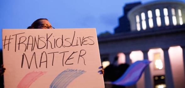 A transgender rights advocate holds a sign that reads '#TransKidsLives Matter' with pink and blue colours underneath as they outside the Ohio Statehouse during a rally against a trans sports ban bill