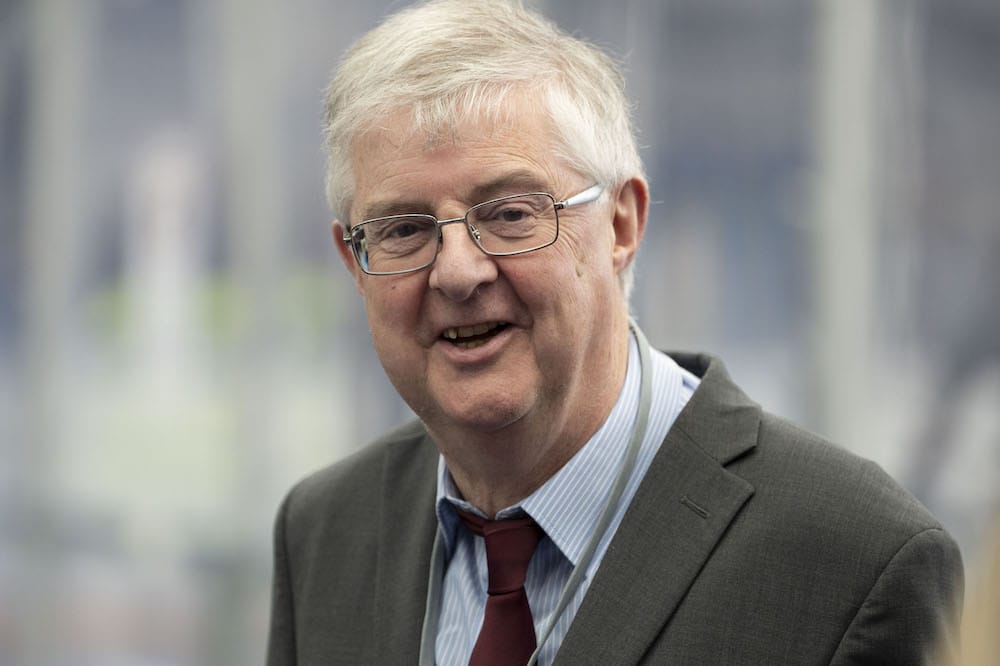 A photo shows first minister of Wales Mark Drakeford wearing a grey suit jacket, white shirt, red tie and glasses as he smiles at the camera