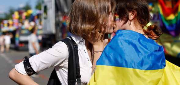 Two women, one of them wrapped into a Ukrainian flag, kis