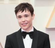 Elliot Page smiles for the camera while wearing a bow tie, white button up shirt and black suit jacket and standing in front of a pale off-white background