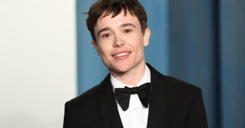 Elliot Page smile at the camera while wearing a white button up shirt, a black bow tie and black suit jacket