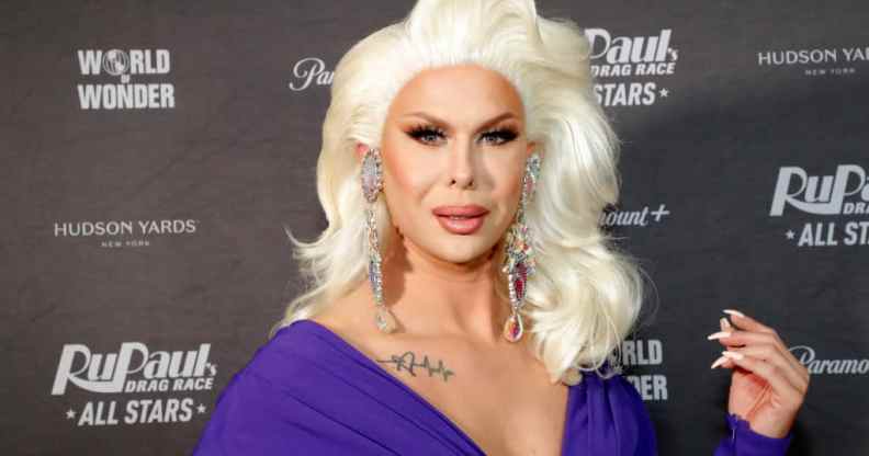 Semi-close up photo of Trinity the Tuck attending the 'Drag Race All Stars' premiere. They are wearing a platinum blonde wig, and a dark purple dress.