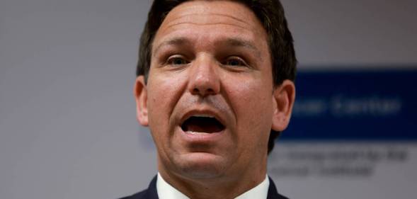 Florida governor Ron DeSantis wears a white button up shirt, light blue tie and dark blue jacket as he speaks to someone off camera