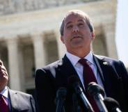 Texas attorney general Ken Paxton wears a white button up shirt, red tie and black suit jacket as he speaks into a microphone