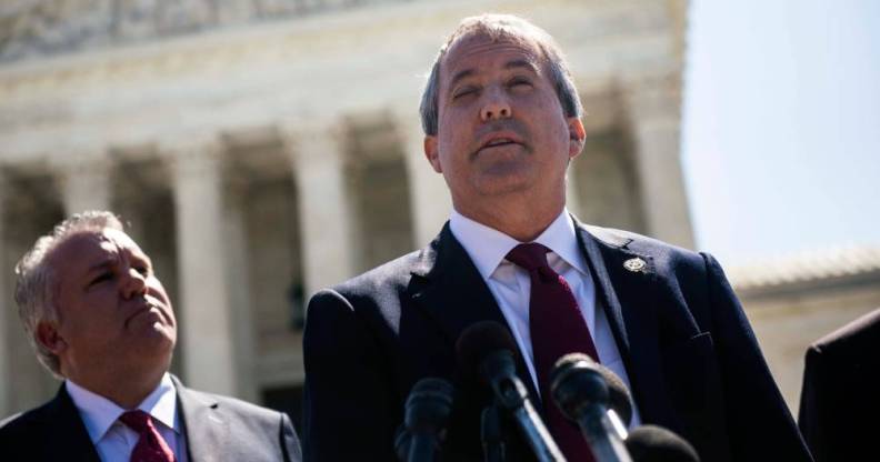 Texas attorney general Ken Paxton wears a white button up shirt, red tie and black suit jacket as he speaks into a microphone